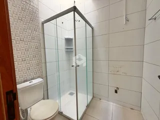Interior de um banheiro com box de vidro e azulejos brancos.