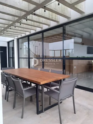 Mesa de madeira com cadeiras em um ambiente com grandes janelas de vidro.