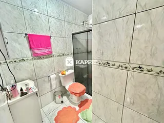 Banheiro com revestimento de azulejos brancos e box de vidro.