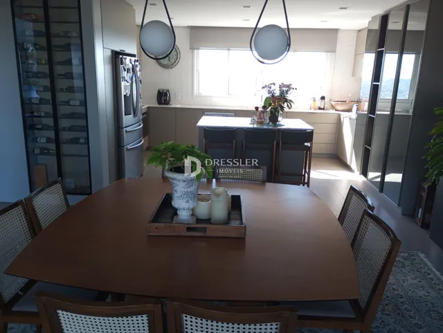 Vista de uma sala de jantar com mesa de madeira e ambiente de cozinha moderna.