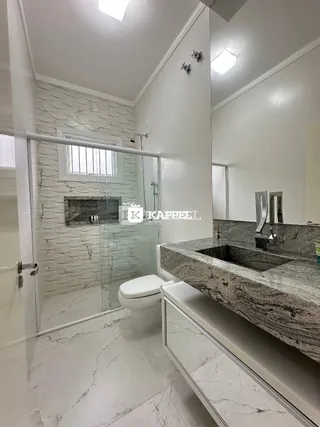 Banheiro com revestimento de mármore e box de vidro.
