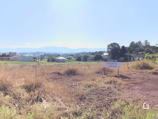 Paisagem de campo com vegetação seca e algumas construções ao fundo.