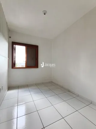 Vista interna de um cômodo com piso de cerâmica branca e janela de madeira.