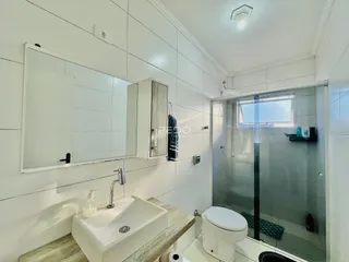 Um banheiro moderno com box de vidro e revestimento branco.
