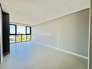 Ambiente interno amplo com piso claro e grandes janelas.