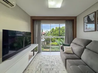 Sala de estar com sofá e vista para o jardim através de uma grande janela.