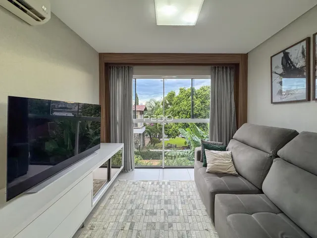 Sala de estar com sofá e vista para o jardim através de uma grande janela.