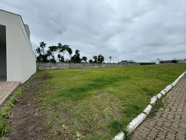 Vista externa do terreno com gramado e muro de contenção.