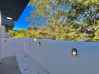 Fachada branca de uma propriedade com vegetação ao fundo sob um céu azul.