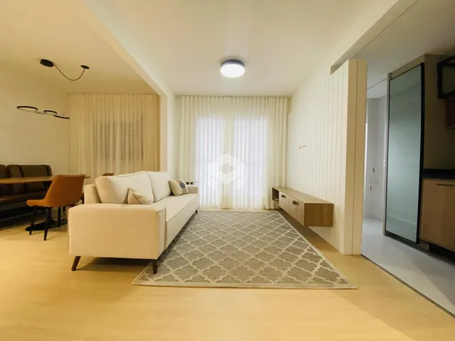 Sala de estar com piso de madeira clara e cortinas brancas.