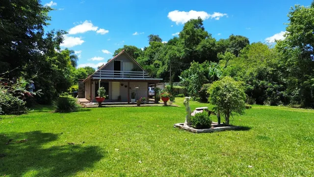 Fachada de uma casa térrea com jardim verde e vegetação densa ao fundo.