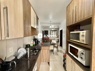 Foto interna de uma cozinha com armários de madeira clara e bancadas escuras.