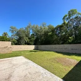Vista externa mostrando um gramado e um muro de contenção em uma propriedade.