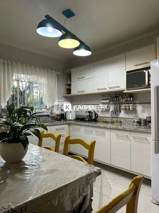Uma cozinha com armários brancos e bancadas claras é visível na imagem.
