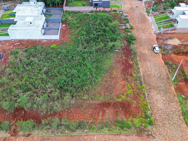 Vista aérea de um terreno com vegetação rasteira e estruturas no fundo.