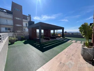 Área externa com piso de grama artificial e pergolado em um apartamento em Lajeado.