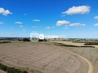 Campo aberto com terra arada sob um céu azul.
