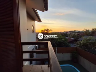 A foto mostra uma varanda com vista para uma piscina ao pôr do sol.