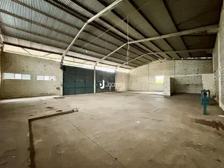 Interior de um grande espaço industrial com teto de estrutura metálica e paredes de tijolo.