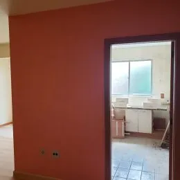 Parede interna com pintura avermelhada e moldura de janela visível.