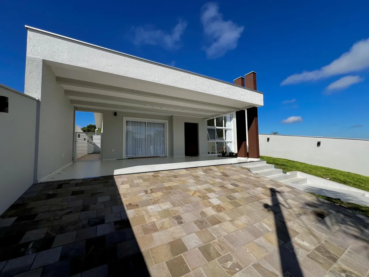 Fachada externa de uma casa moderna com área de lazer pavimentada.