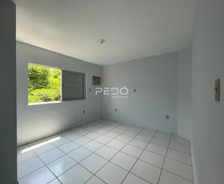 A sala apresenta um piso de cerâmica branco e uma grande janela com vista para a vegetação externa.