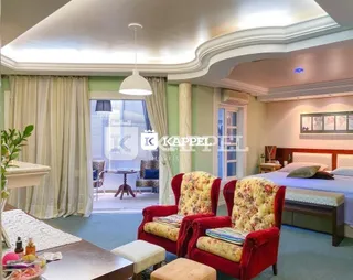 Quarto com cama e poltronas vermelhas e cortinas claras.