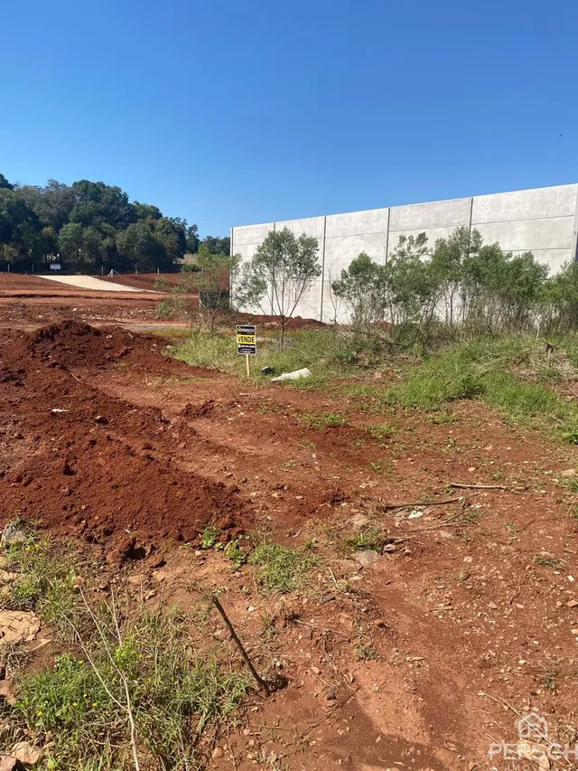 Vista externa de um terreno com terra vermelha e uma parede de concreto.