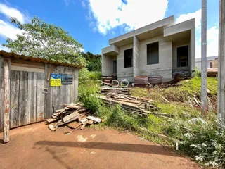 Vista externa de uma residência em construção com cerca de madeira e vegetação ao redor.