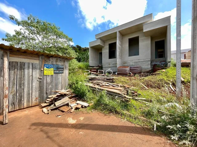 Vista externa de uma residência em construção com cerca de madeira e vegetação ao redor.