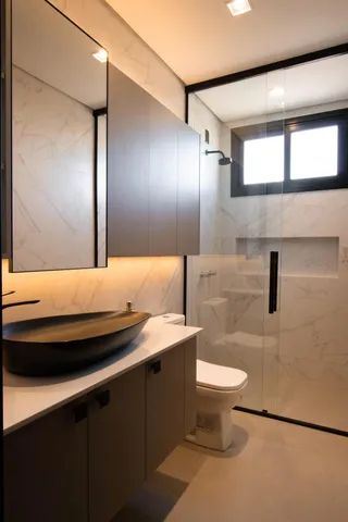 Banheiro moderno com bancada escura e revestimento de mármore nas paredes.