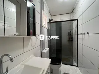 Foto interna de um banheiro com box de vidro e bancada branca.