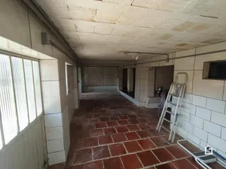 Um corredor interno com piso de tijolos vermelhos e paredes brancas.