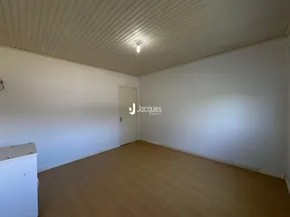 Foto de um cômodo interno vazio com piso de madeira clara e paredes brancas.