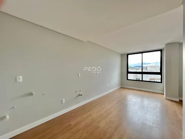 Interior de uma sala de estar com piso de madeira clara e grande janela.