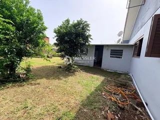 Vista externa de uma residência com jardim gramado e vegetação densa.