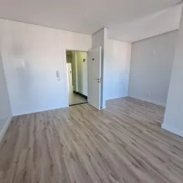 Foto de um ambiente interno com piso de madeira clara e paredes brancas.