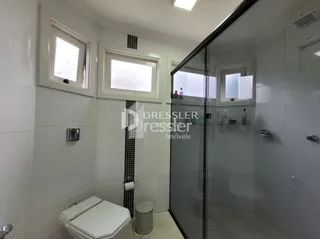 Interior de um banheiro com revestimento branco e box de vidro.