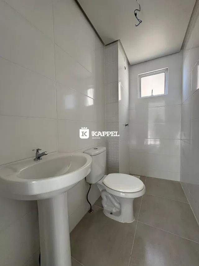 Banheiro com pia e vaso sanitário revestido em azulejos brancos.