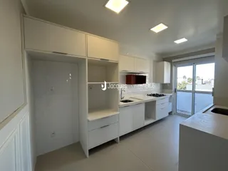 Vista interna de uma cozinha moderna com armários brancos e piso claro.
