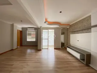 Ambiente interno de uma sala de estar com piso de madeira clara e paredes brancas.