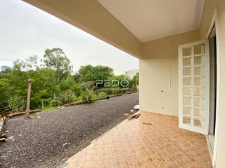 Um corredor interno com piso de cerâmica abre para uma área externa com cascalho.