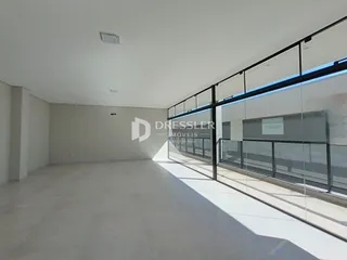 Imagem de um ambiente interno amplo com piso claro e grandes janelas.