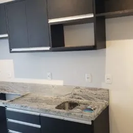 Vista de armários escuros e bancada de granito em uma cozinha.