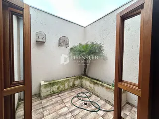 Vista de um pátio externo com paredes brancas e piso de cerâmica.
