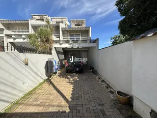 Vista externa de um pátio com piso de tijolos e muro branco.