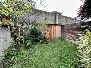 Vista externa da propriedade com muro de tijolos e vegetação densa.