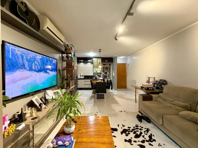 Sala de estar com televisão e móveis em um apartamento em Lajeado.