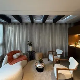 A sala de estar apresenta cortinas claras e um teto com vigas escuras.