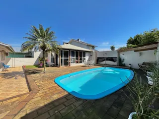 Vista da fachada de uma residência com piscina e área externa pavimentada.